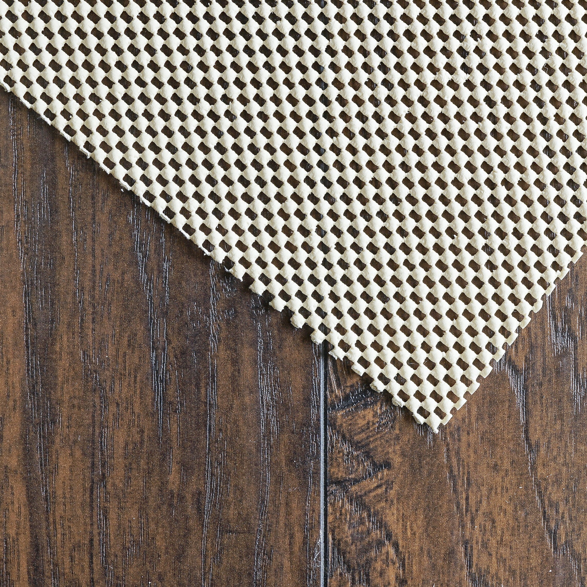 Texture close-up of ivory non-slip rug pad open grid over wood planks